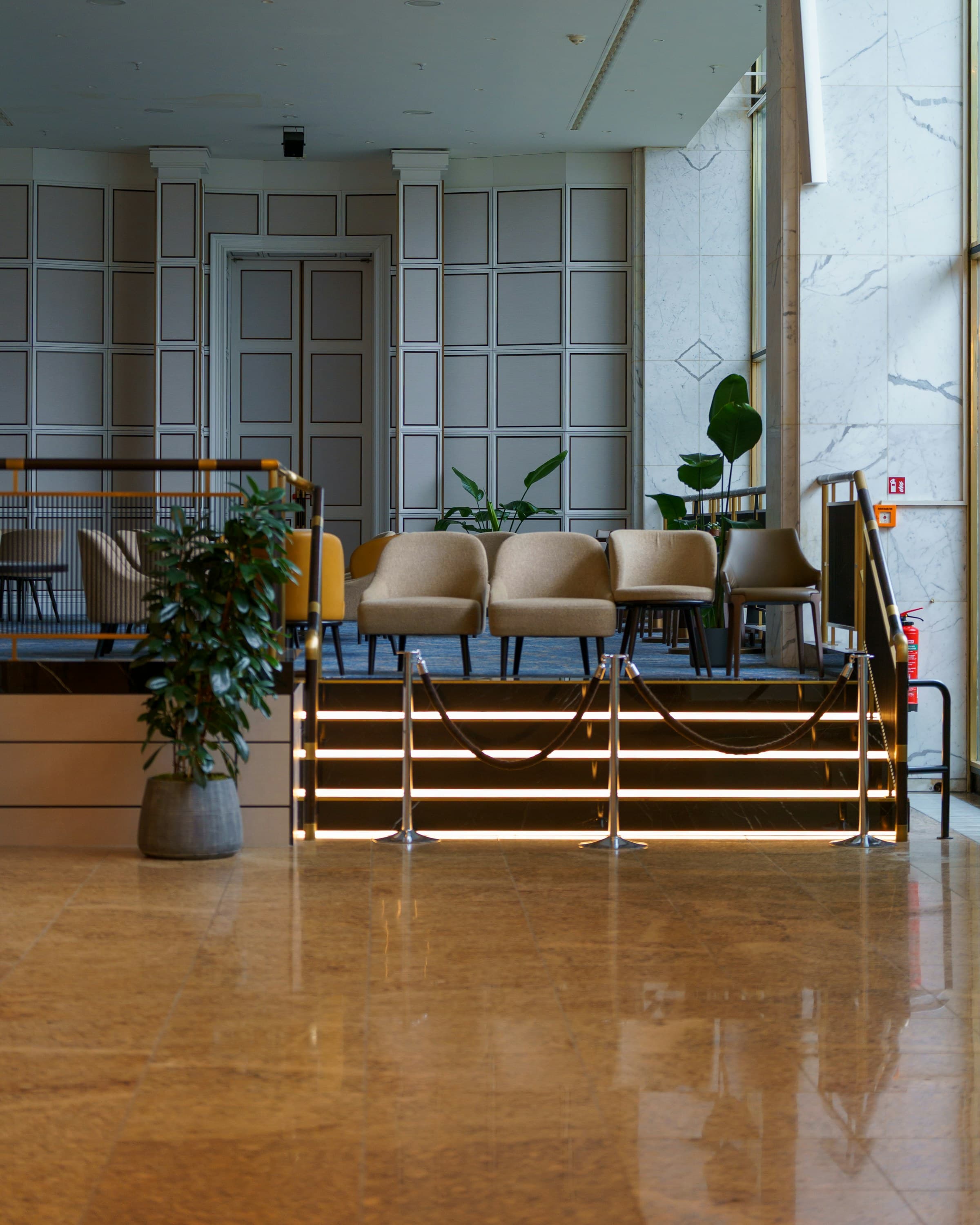 A hotel lounge in the evening -- warm marble surfaces and low gold lighting, seating arranged for guests to gather